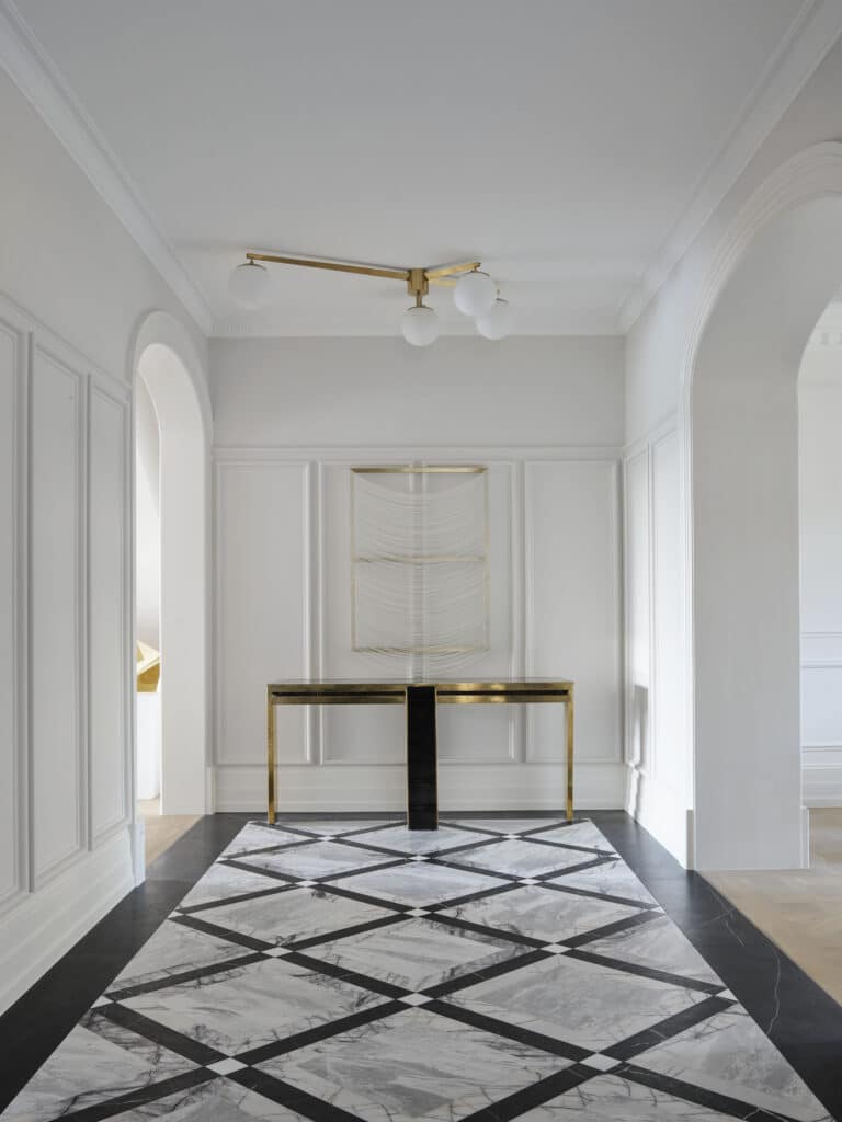 Grand entry foyer of Matchpoint House Strathfield renovated by Duet, with a dramatic black and white diamond-pattern marble floor, white panelled walls with Intrim SK173 skirting, arched openings with custom curved architraves and a brass console table beneath a textile artwork