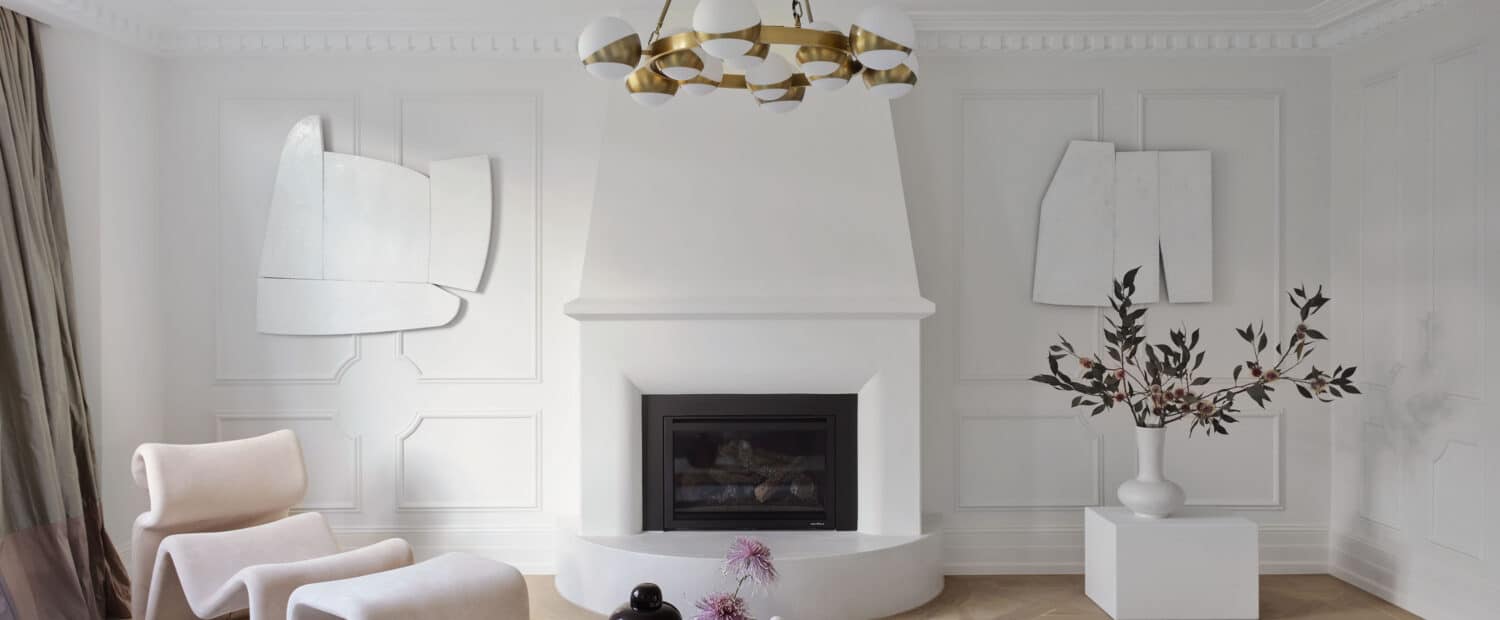 Living room at Matchpoint House Strathfield, featuring a sculptural curved white rendered fireplace, white Intrim-panelled walls with deep cornices, a brass globe chandelier, blush sculptural chairs and a marble coffee table on herringbone oak floors