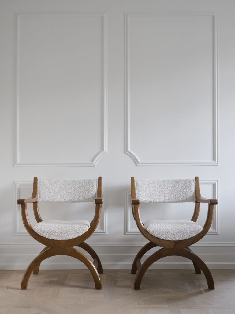Pair of walnut Curule chairs with boucle upholstery in Matchpoint House Strathfield, set against white wall panelling featuring Intrim CR84 dado rail and SK173 skirting with arch-top panel moulding detail and herringbone oak parquetry floor