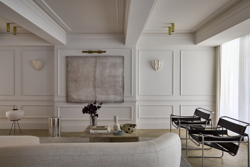 Formal living room featuring full-height wall panelling in Intrim IN32 and CR22, paired black leather Wassily chairs and a travertine coffee table beneath a coffered ceiling