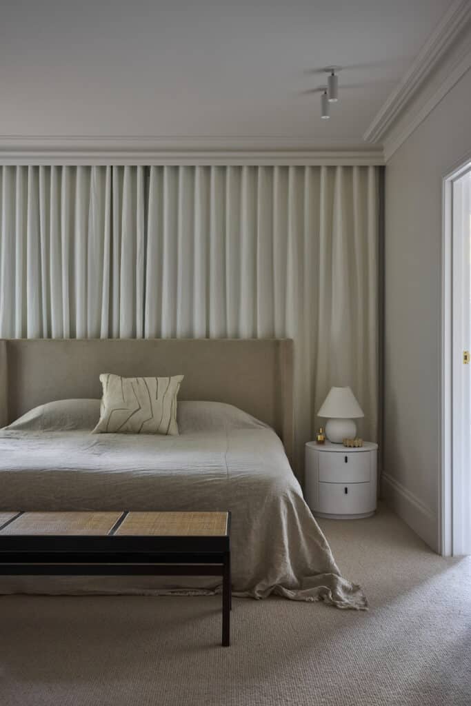 Serene main bedroom with an upholstered linen bed, floor-to-ceiling sheer curtains and cane bench, finished with Intrim SK498 skirting and architrave in a neutral palette