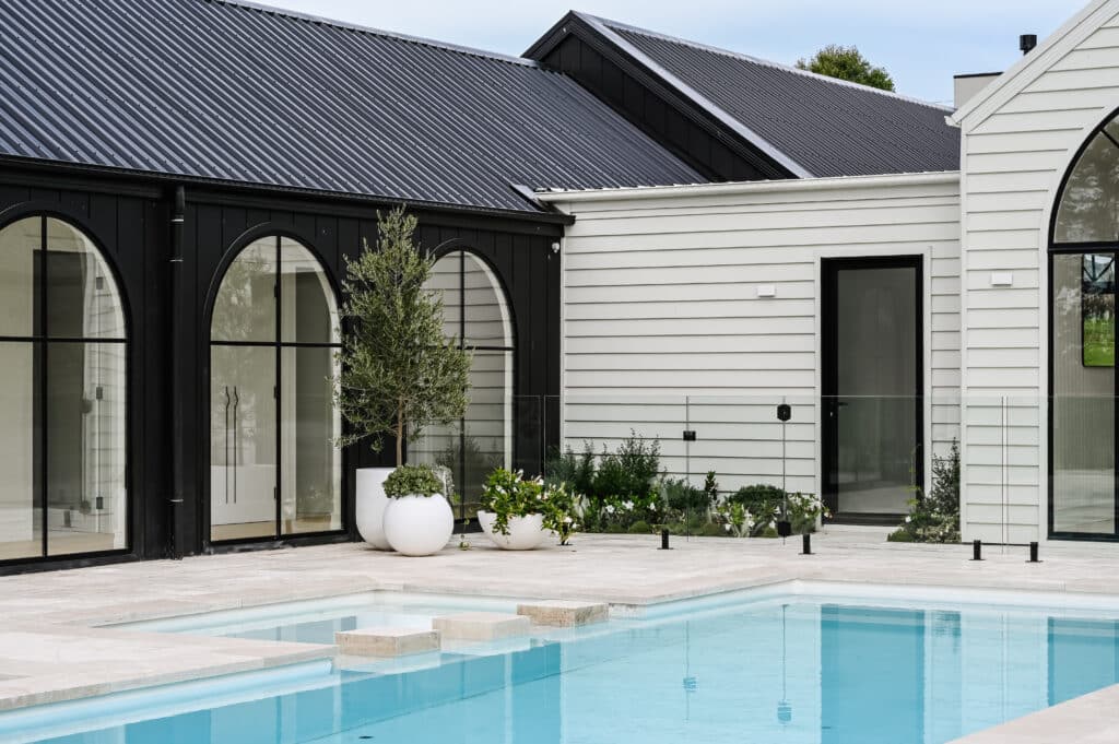 Modern farmhouse courtyard with swimming pool, arched steel-framed windows, weatherboard cladding and a contemporary black-and-white exterior.