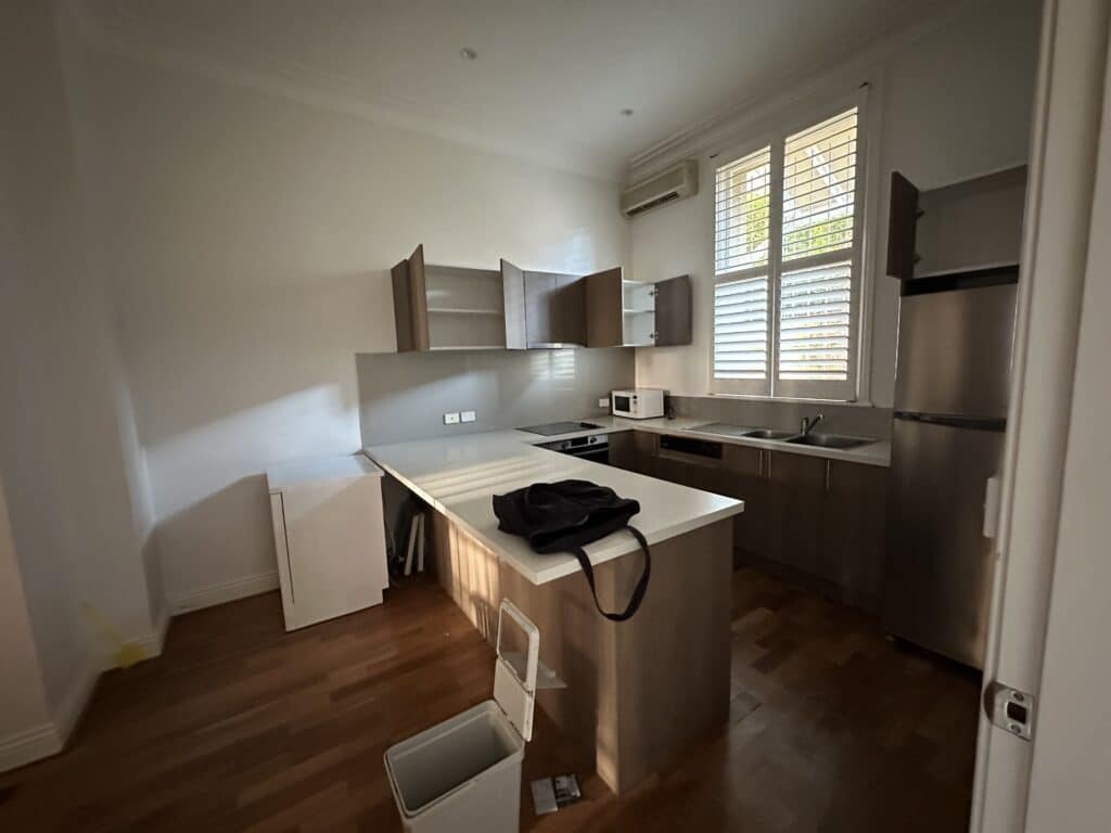 A plain, commercial-style terrace kitchen with a peninsula bench and no period features.