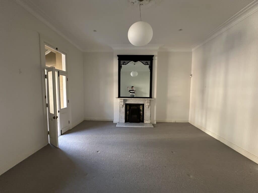 A white-walled living room with grey carpet and a marble fireplace.