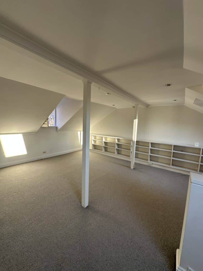 A carpeted attic with sloped ceilings and low white shelving.