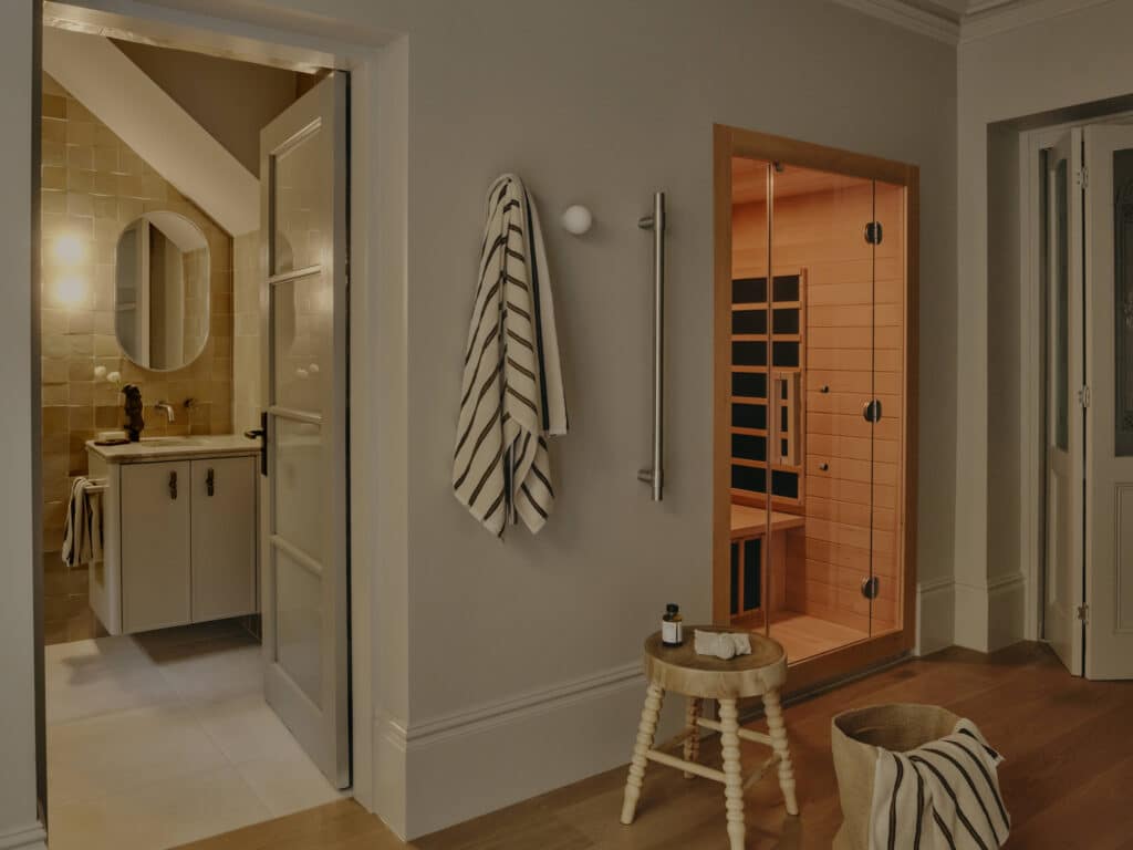 Terrace wellness room with a timber-lined infrared sauna behind glass, a glazed door open to a bathroom with amber wall tiles, white skirting and oak floors.