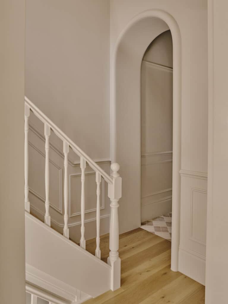 Restored staircase with wall panelling and custom plaster archway framing the entry.