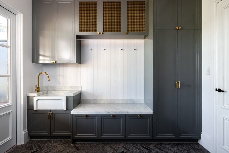 Custom mudroom cabinetry with shaker-profile doors, brass hardware and marble utility sink